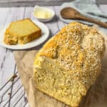 A loaf of cheddar cheese quick bread with a slice of the bread in the background on a plate.