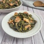 Collard Greens made in dutch oven in a white bowl with more collards in the background.