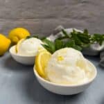 Two white bowls of sweet lemon sherbet garnished with a mint sprig and lemon slice.