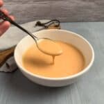 A hand holding up a spoon with smash burger sauce dripping into a bowl of the sauce.