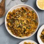 A large white bowl of ground beef and spinach pasta topped with shredded parmesan cheese with more bowls of the pasta and cheese on the side.